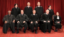 Supreme Court Justices posing for a photo in two rows, in their court attire with a red background