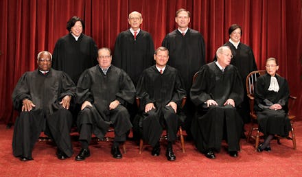 Supreme Court Justices posing for a photo in two rows, in their court attire with a red background