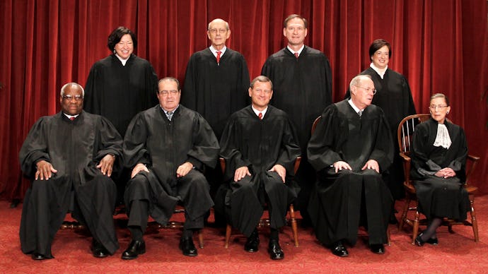 Supreme Court Justices posing for a photo in two rows, in their court attire with a red background