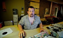 A man in a checkered shirt sitting at his work desk, with his e-mail on his computer, looking toward...