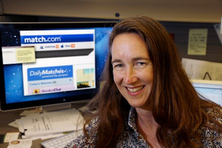 A woman taking a selfie with her computer in the background with an open Dating site in the browser