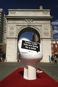 A toilet with the sign today 2000 kids are dying for a toilet placed in front of the Arc de Triomphe