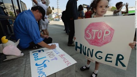 A kid holding a sign that says "stop hunger" and a man in the background with a poster that says foo...
