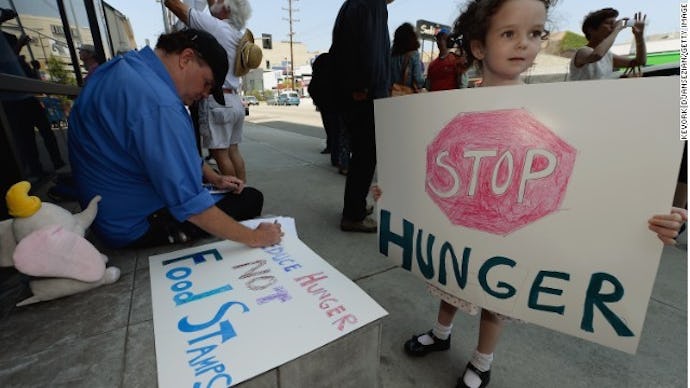 A kid holding a sign that says "stop hunger" and a man in the background with a poster that says foo...