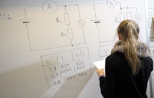 A student in Finland drawing a table and calculating fields on a whiteboard