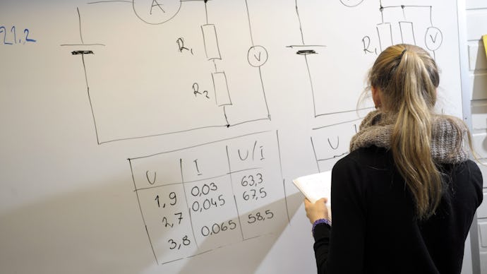 A student in Finland drawing a table and calculating fields on a whiteboard
