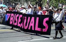  A crowd marching and holding a large black sign with "Bisexuals" written on it in purple 