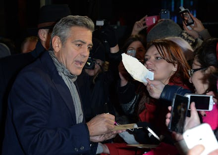 George Clooney in a black blazer and grey scarf giving autographs to fans