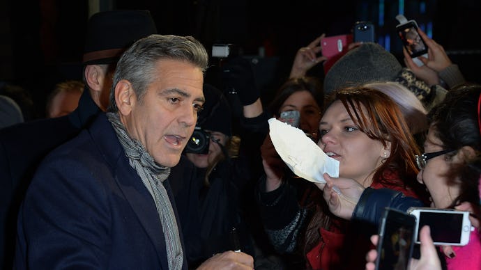 George Clooney in a black blazer and grey scarf giving autographs to fans