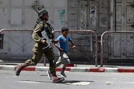 IDF soldier and a kid running across the street while tensions rise in the West Bank
