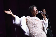 Aretha Franklin in a white floral dress and a white coat performing
