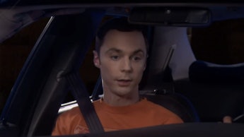 Sheldon Cooper in an orange shirt sitting in the passenger seat of a car