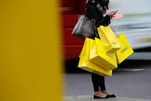 A woman with her hands full of shopping bags standing on the street, waiting to cross the road