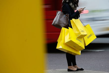 A woman with her hands full of shopping bags standing on the street, waiting to cross the road