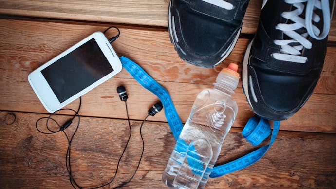 A pair of sneakers next to blue measuring tape a water bottle and a phone with headphones in it