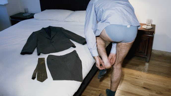 A man wearing a shirt and underwear getting dressed in a bedroom