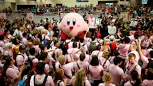 A Kirby mascot dancing surrounded by a crowd of people dressed in pink 