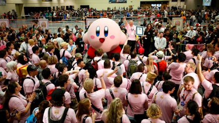 A Kirby mascot dancing surrounded by a crowd of people dressed in pink