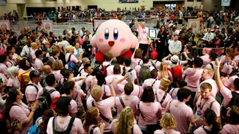 A Kirby mascot dancing surrounded by a crowd of people dressed in pink 