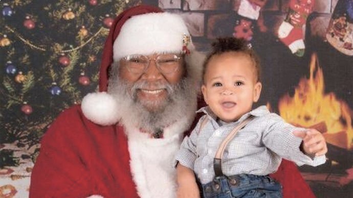 The black New Orleans Santa posing with a little child on his lap, both smiling