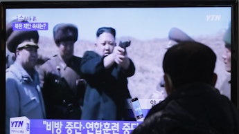 A man watching Kim Jong-un on tv, where he is holding a gun, and his companions standing on his side...