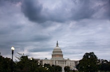 The US Capitol in Washington with grey clouds above and surrounded by trees 