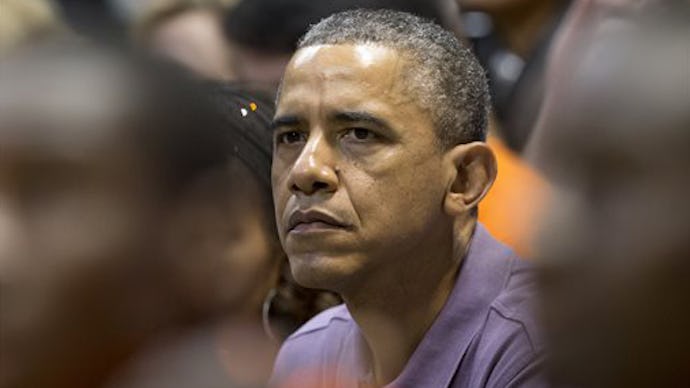 Former President Barack Obama sitting in a crowd wearing a blue button up shirt looking worried