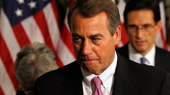 John Boehner in a black suit, and a white shirt and the American flag in the background