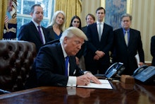 Donald Trump signing a paper with a group of people standing behind him