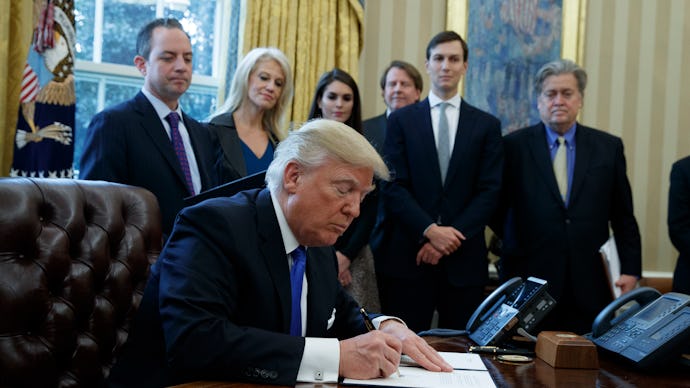 Donald Trump signing a paper with a group of people standing behind him
