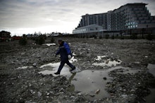 A man walking through a soaked field full of puddles with an apartment building behind him in Sochi