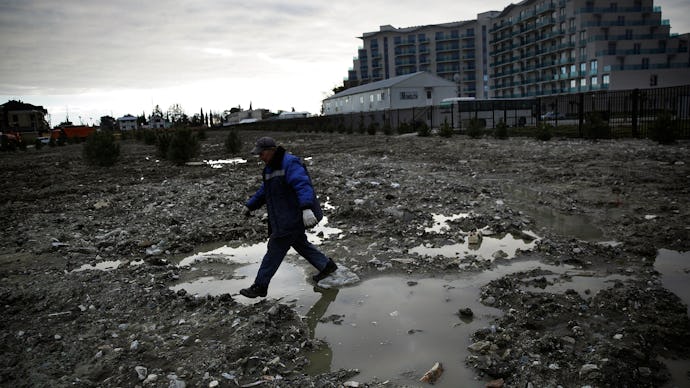 A man walking through a soaked field full of puddles with an apartment building behind him in Sochi