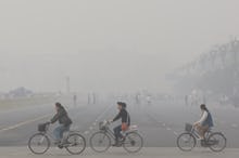 Smog-filled city of Zhengzhou and tree people driving their bikes trough it, with some others not be...