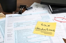 A post it note that says tax deductions on a stack of tax forms