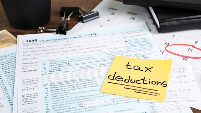 A post it note that says tax deductions on a stack of tax forms