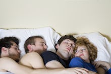 Three men and a woman sleeping together in a bed