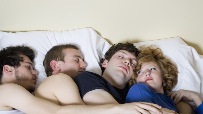 Three men and a woman sleeping together in a bed