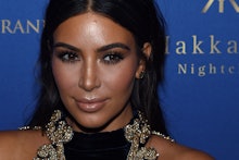 A close-up portrait of Kim Kardashian in a black-gold dress at a red carpet event