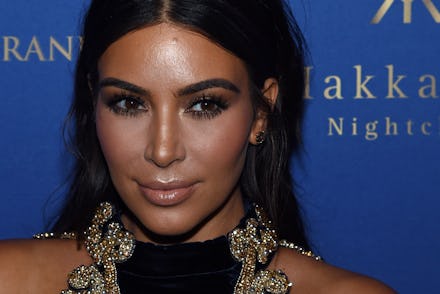 A close-up portrait of Kim Kardashian in a black-gold dress at a red carpet event