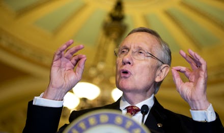 Harry Reid with his hands raised giving a speech behind a podium