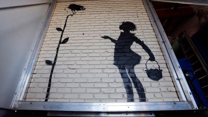 A graffiti on a brick wall; a girl and a surveillance camera by Banksy that was sold for $209,000