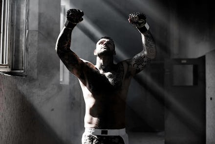 A boxer with his arms raised and looking up in a pair of shorts in a dark room