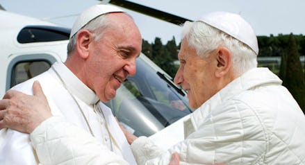 Pope Francis and Pope Benedict XVI greeting each other in front of a helicopter