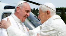 Pope Francis and Pope Benedict XVI greeting each other in front of a helicopter