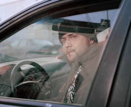 A man sitting in his car smoking a cigar while wearing a coat and a beanie