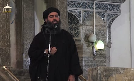 Abu Bakr Al-Baghdadi standing at a microphone, speaking