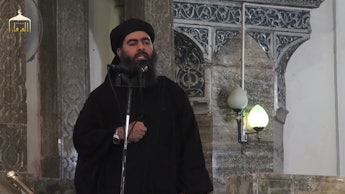 Abu Bakr Al-Baghdadi standing at a microphone, speaking
