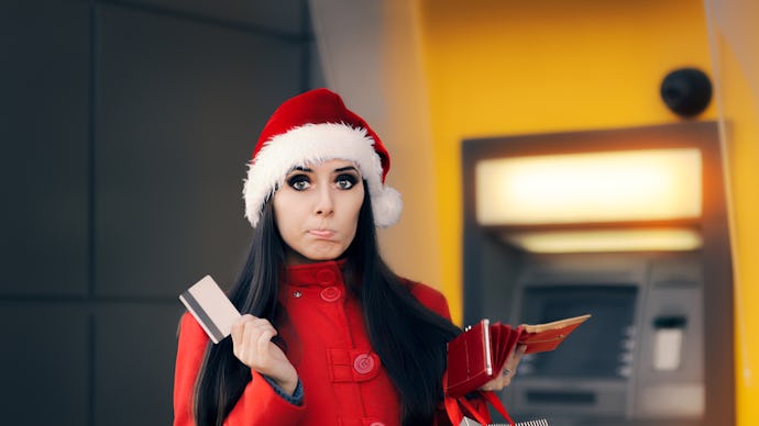 A woman in a red jacket and a christmas hat holding her credit card in front of an ATM with a confus...