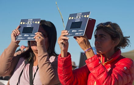 Two women standing outside using solar eclipse viewing equipment to look at the passing solar eclips...