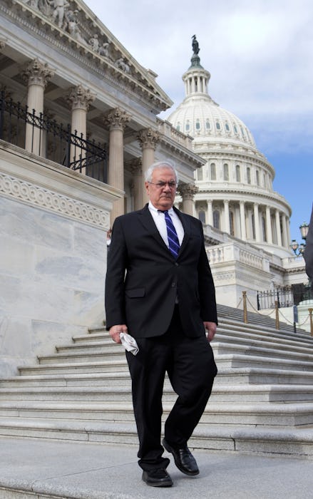 Barney Frank in a black suit, a white shirt, and a navy tie walking down the steps in front of the U...